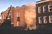 Smoke pours from the windows overlooking the small courtyard between the north and south wings of the school. When firemen arrived, there was a seven foot high iron picket fence blocking entrance to the courtyard. Firemen used valuable time breaking down the fence before they could begin rescue operations from room 211.